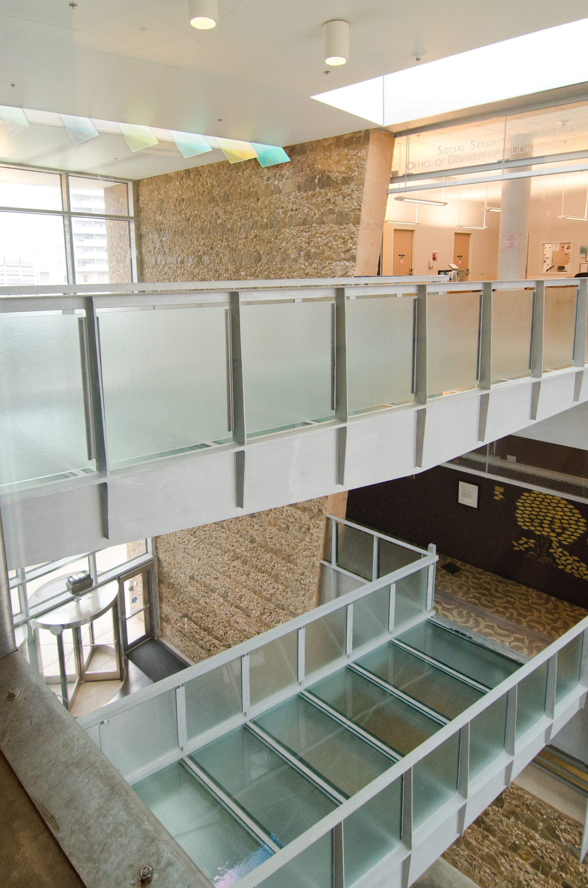 Modern atrium with glass-railed walkways, frosted panels, brick walls, and staircases overlooking a lower level