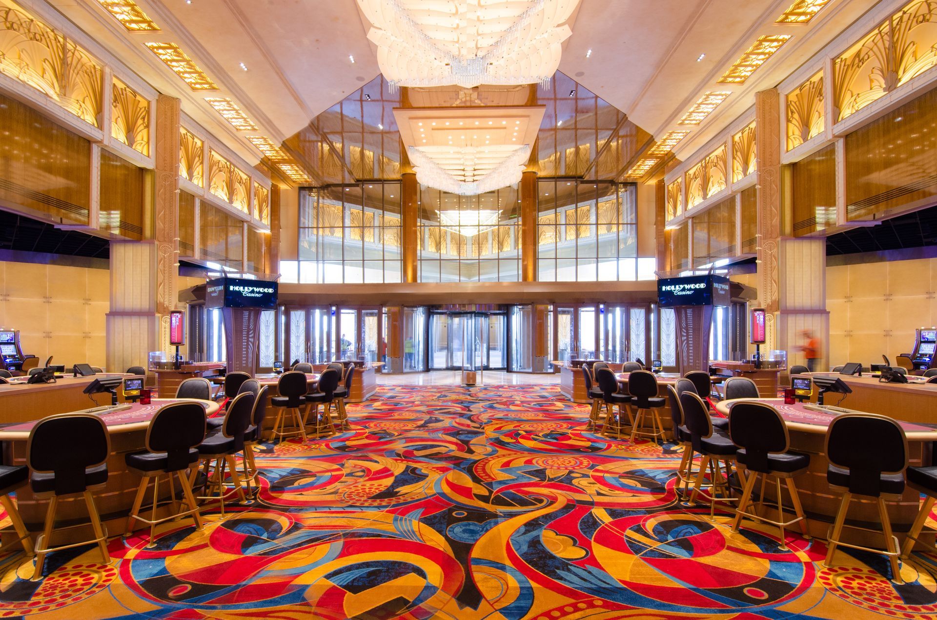 Bright casino floor with colorful carpet, slot machines, gaming tables, and high ceilings under warm lights