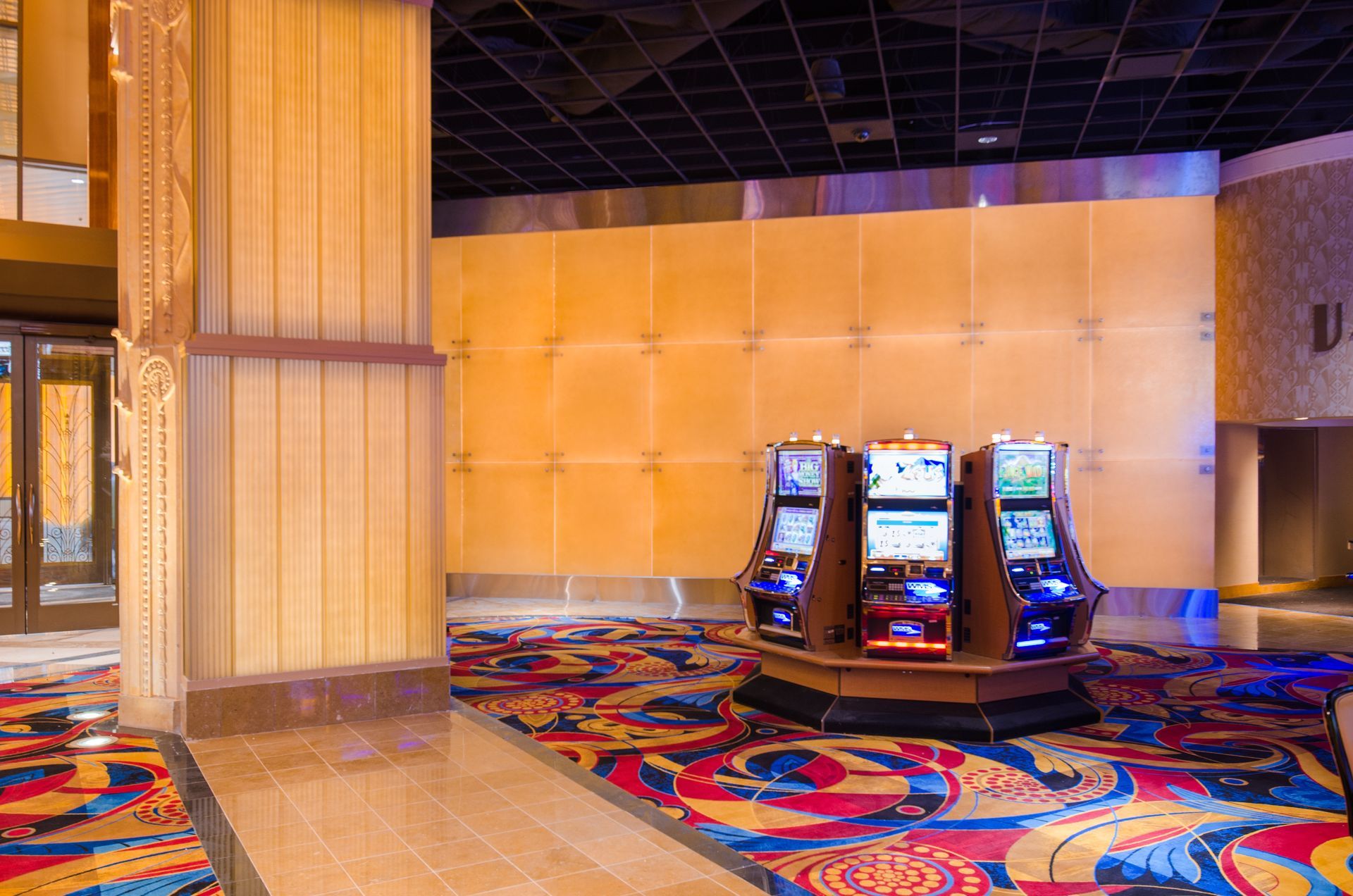 Casino floor with colorful carpet and three illuminated slot machines against beige walls
