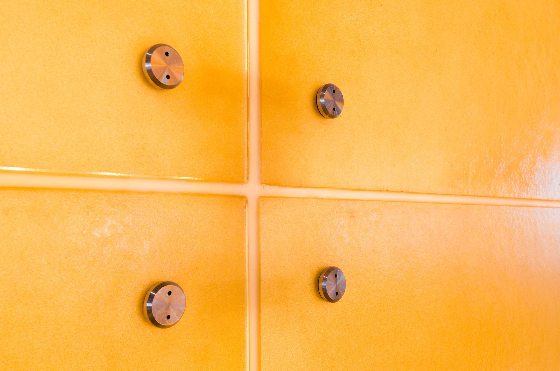 Orange tiled wall with four round metal fixtures arranged in a square pattern