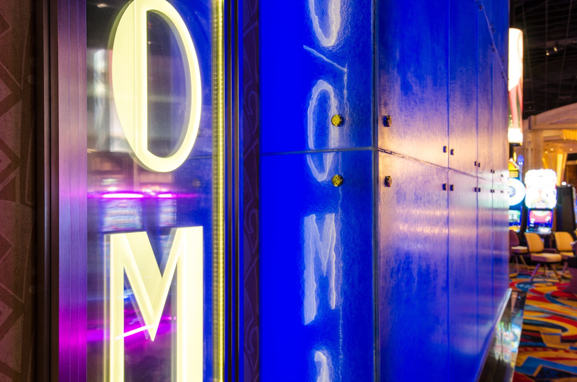 Neon-lit blue wall with partial sign letters and colorful lights in a nightlife hallway