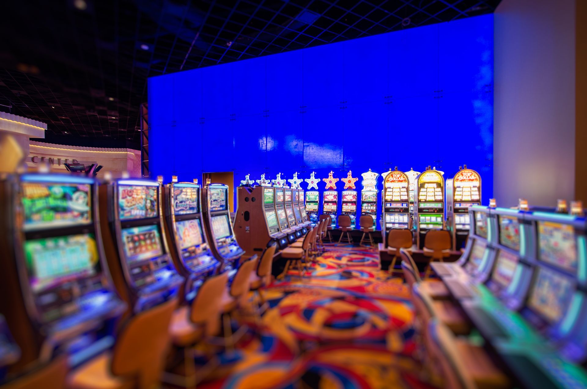 Rows of slot machines in a colorful casino with a bright blue wall behind them