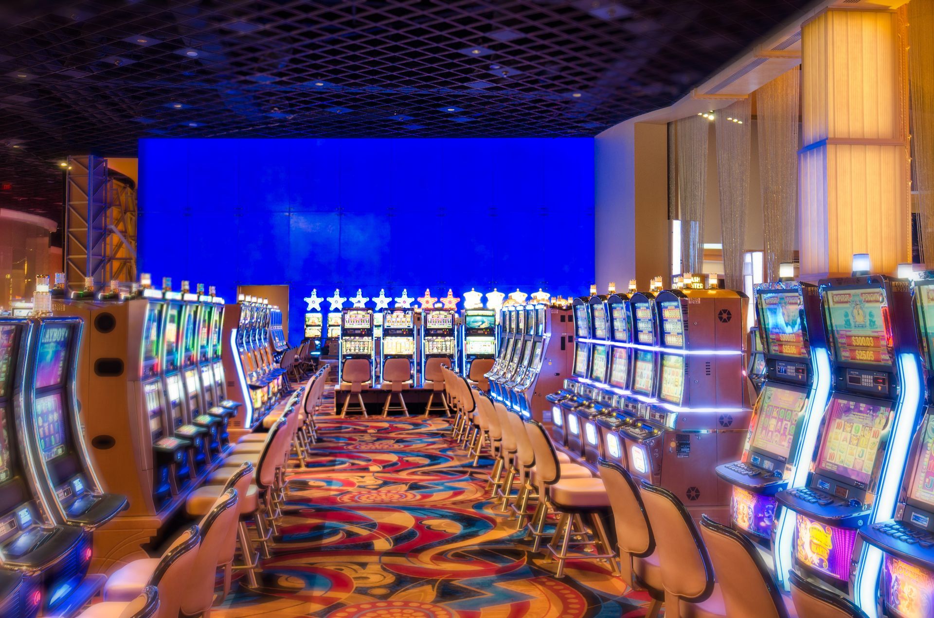 Bright casino floor with rows of colorful slot machines and a vivid blue wall display