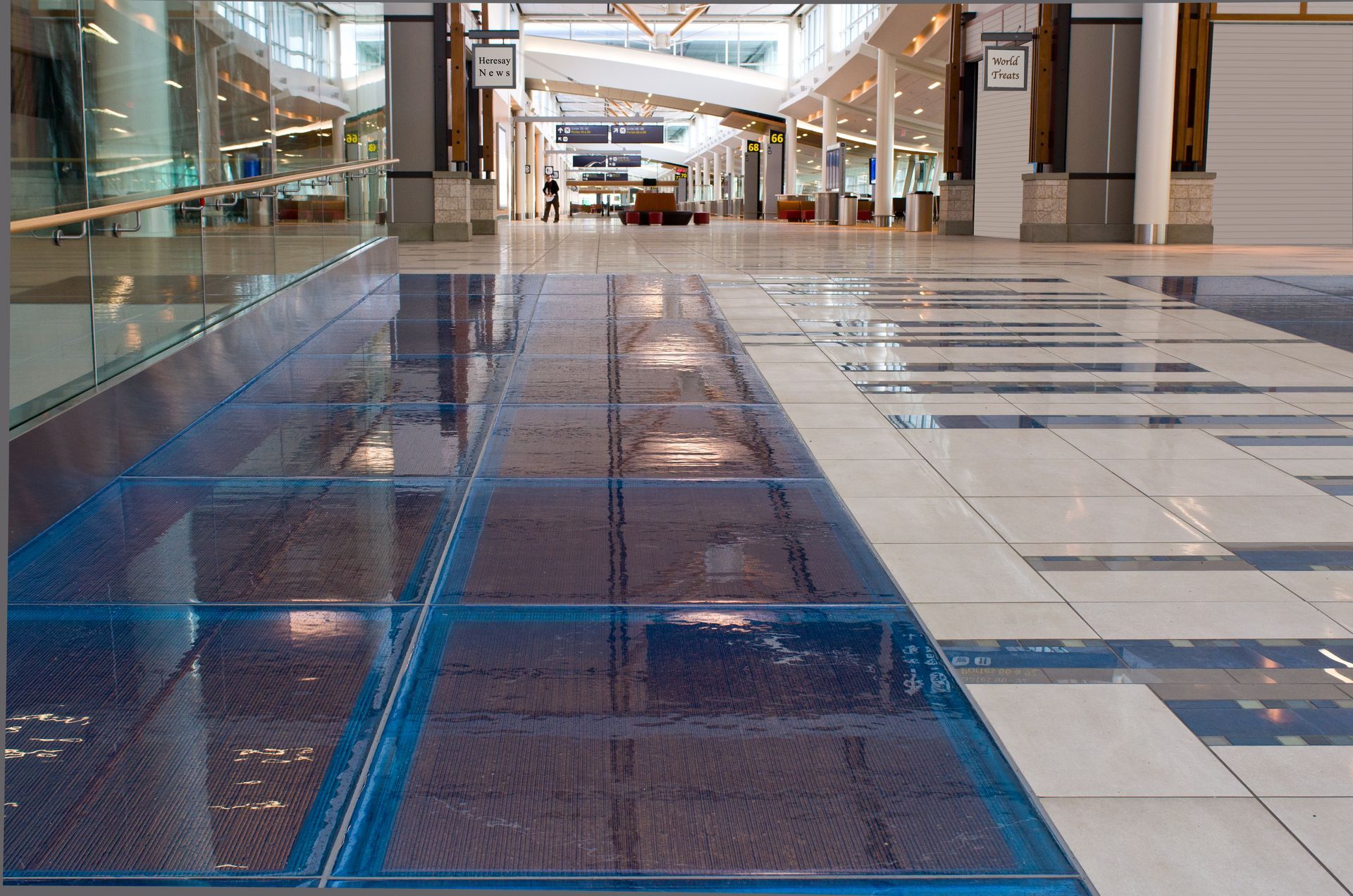 Empty indoor mall corridor with glossy blue and beige tiled floor and storefronts in the distance