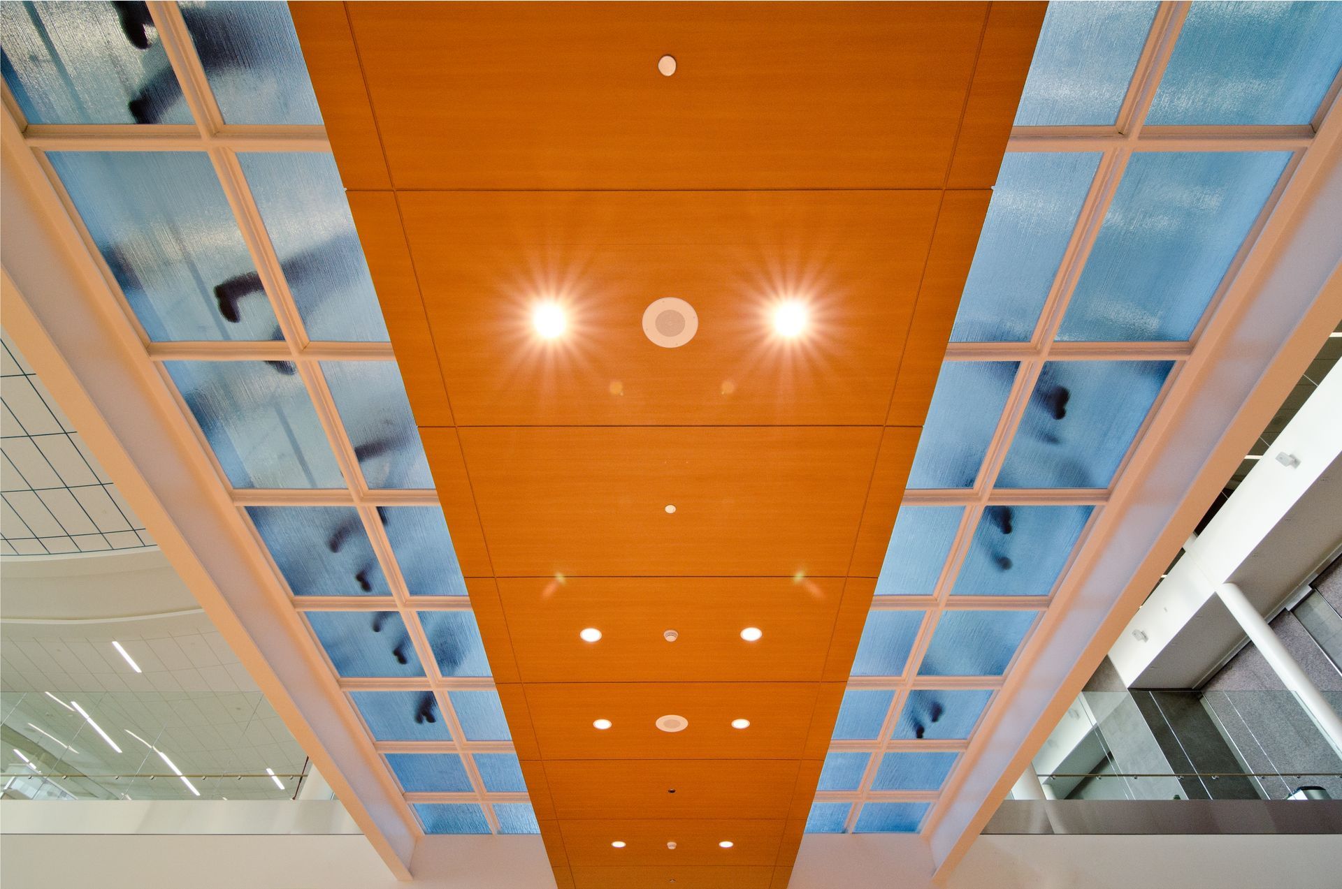 Orange ceiling panel with recessed lights and skylights in a modern interior