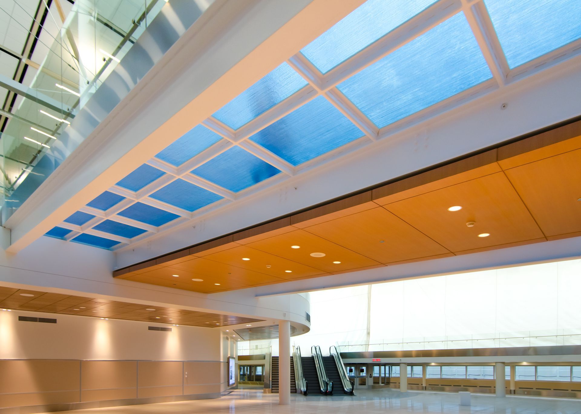 Modern airport terminal with a skylit ceiling, orange accents, and large windows overlooking the tarmac