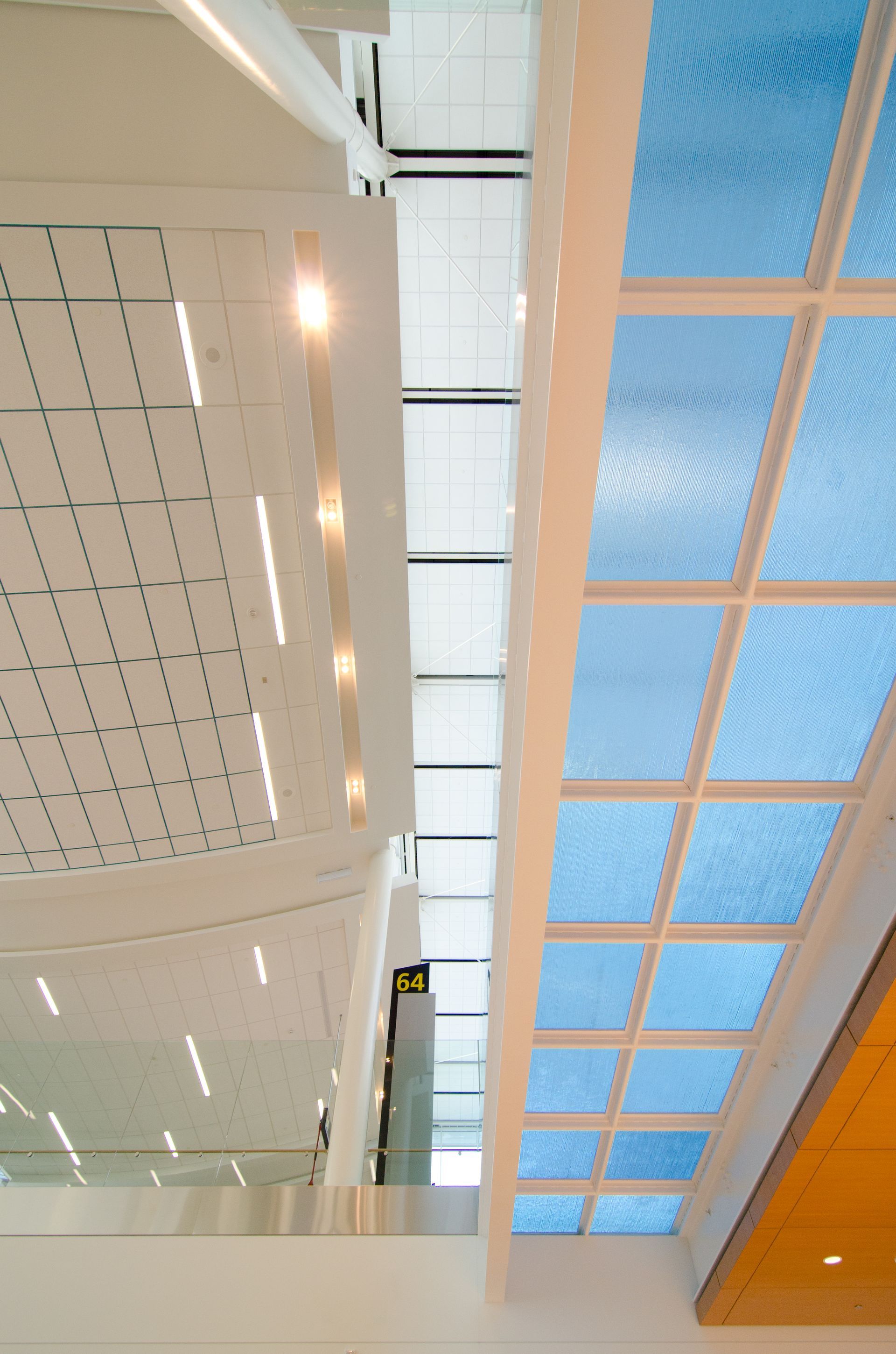 Modern interior with white ceiling panels and blue grid skylight above orange accents