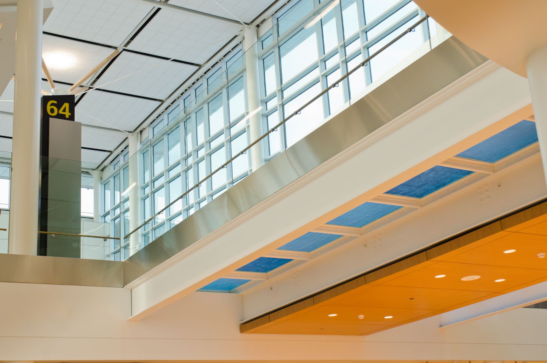 Interior of a modern airport concourse with glass windows, skylight, and gate 64 sign