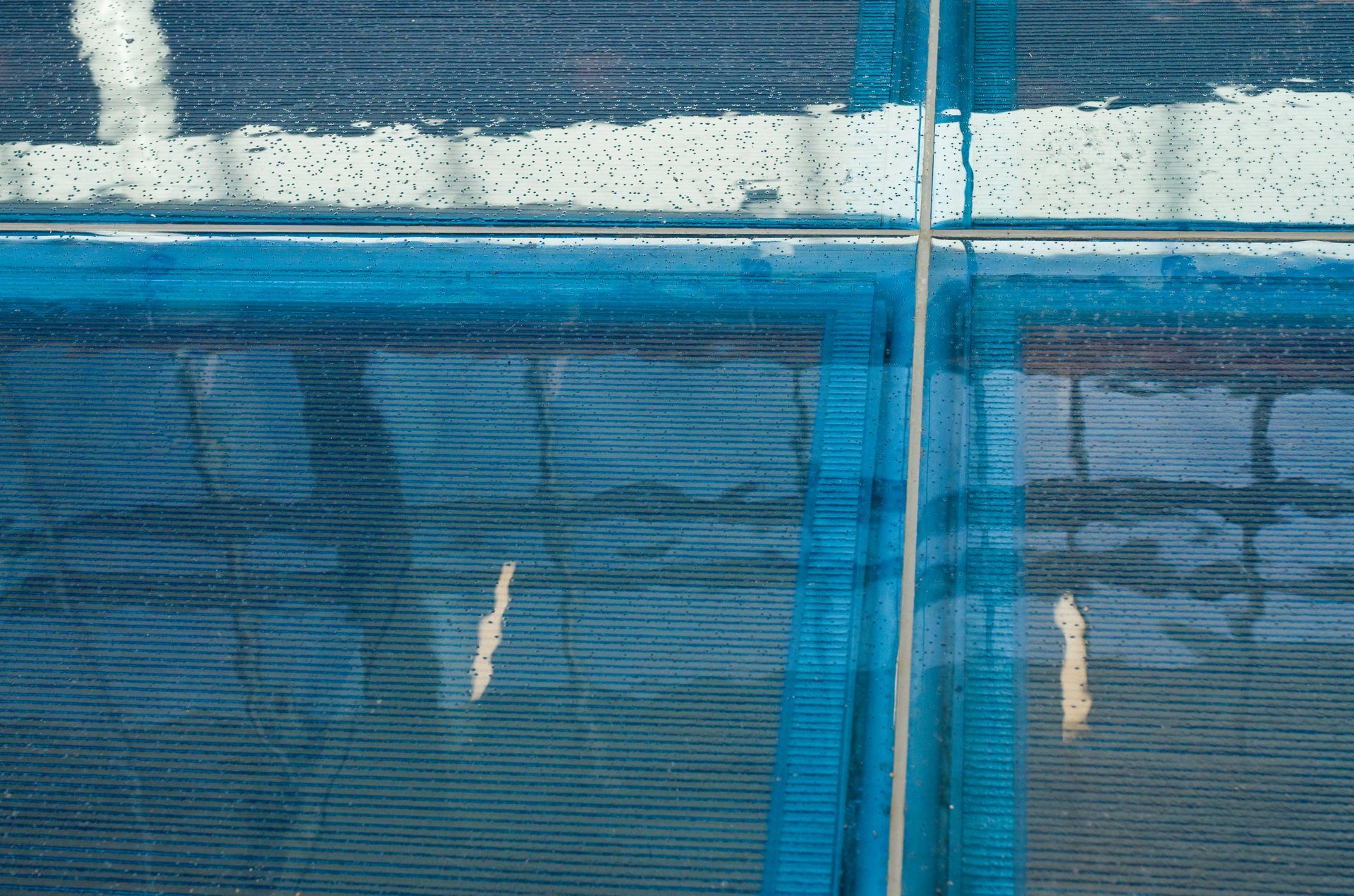 Blue mesh fence with a vertical seam and white wall behind it