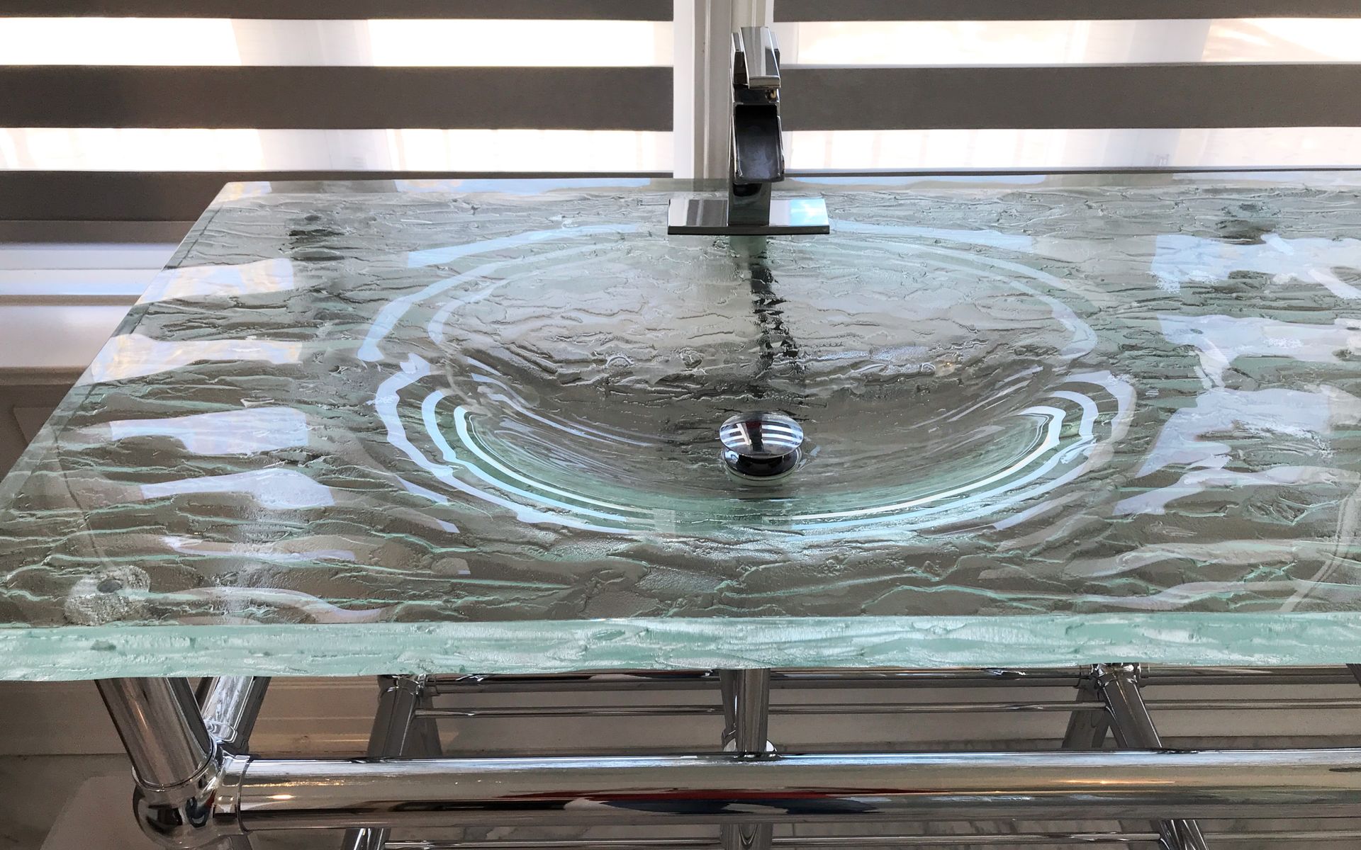 integral bowl Glass countertop with a circular basin, chrome faucet, and drain.