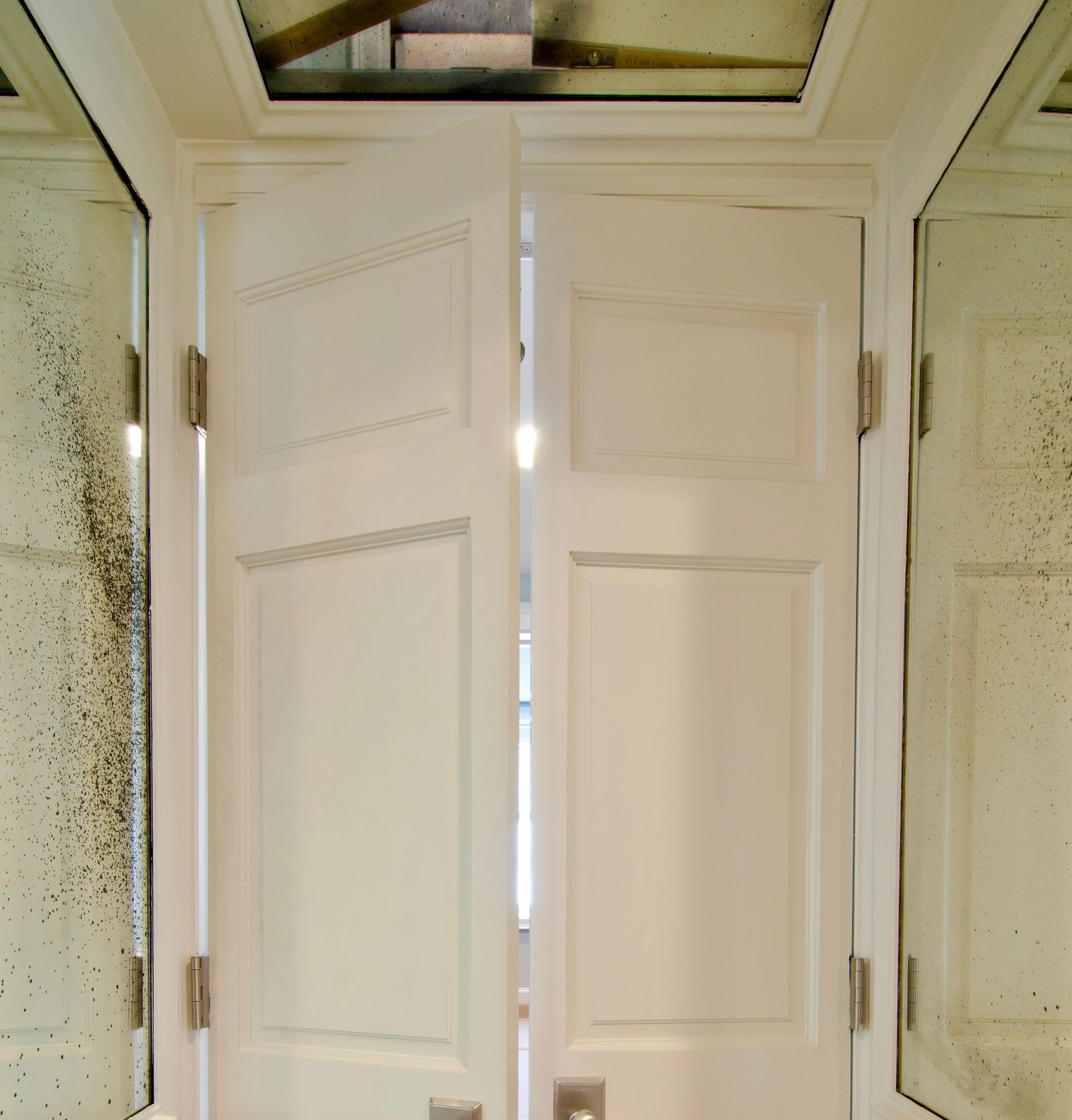 White, paneled double doors slightly ajar, set in an antique mirrored entryway with an antique mirror panel on the ceiling.