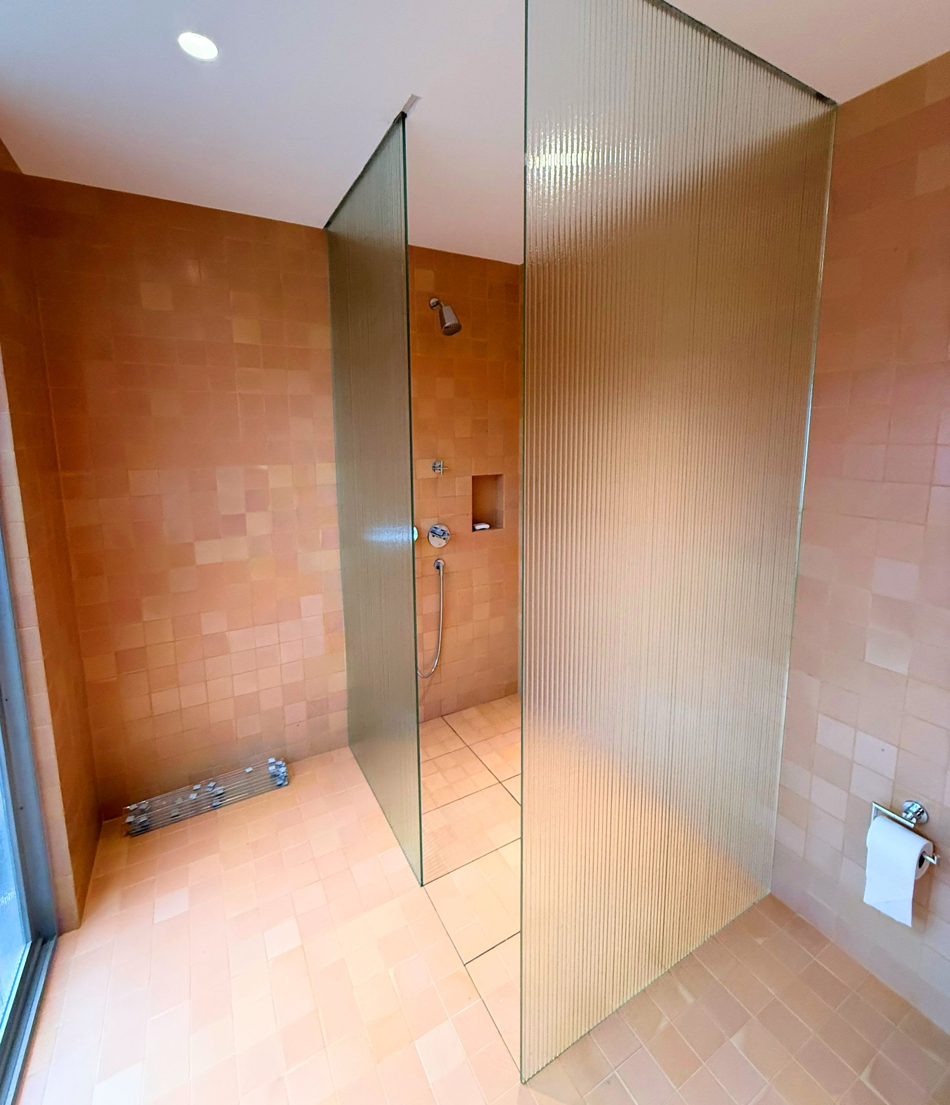 Shower stall with terracotta walls, fluted glass panels, and chrome showerhead.