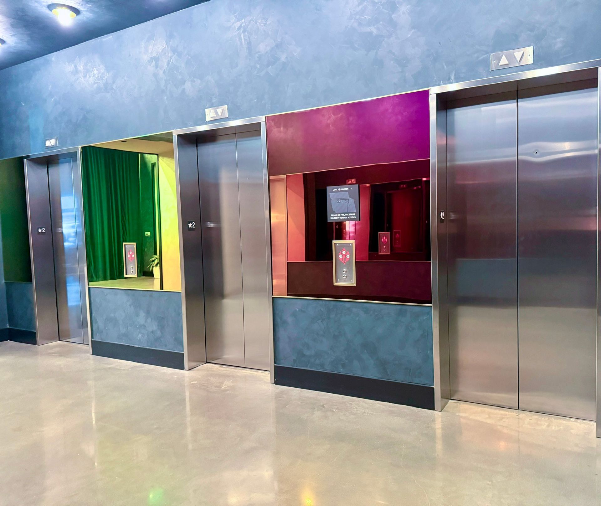 Four elevator doors with colorful accent glass: green, purple and red, and two plain stainless steel.