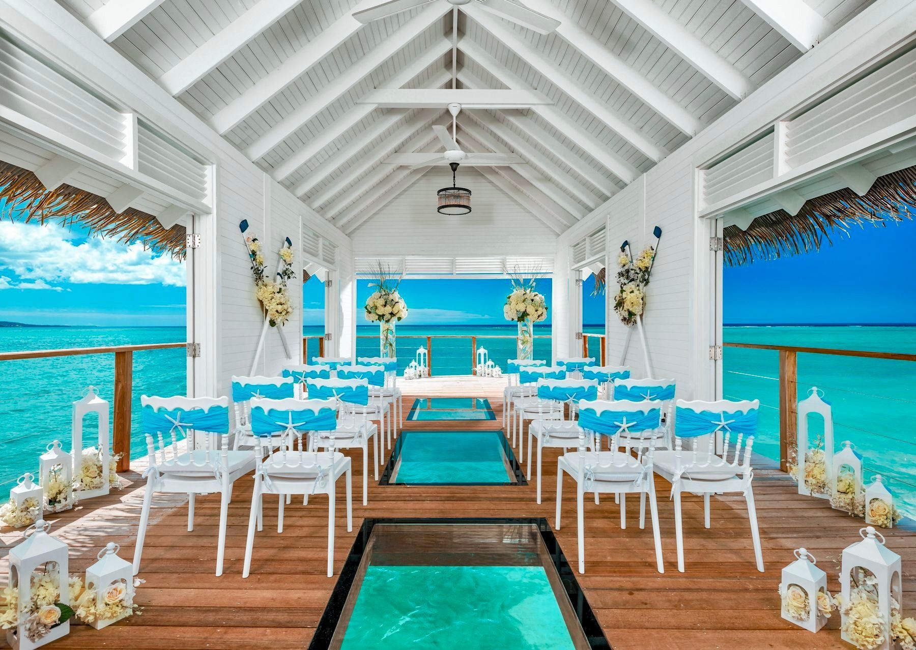 Beachside wedding aisle with white chairs, turquoise runner, and ocean views under a white pavilion