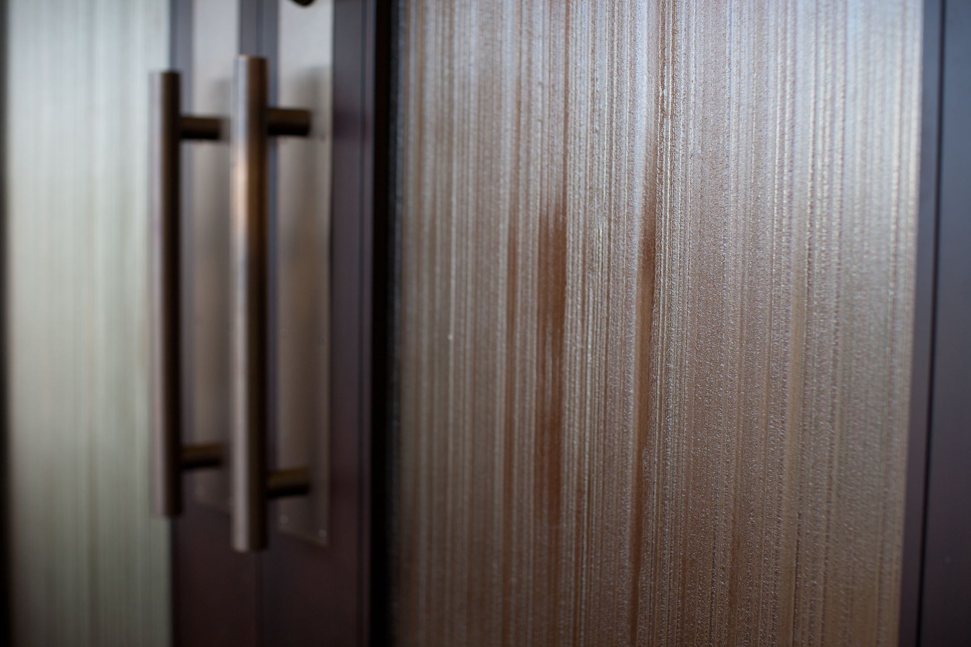 Close-up of a textured glass door with vertical grain texture and a metal handle.