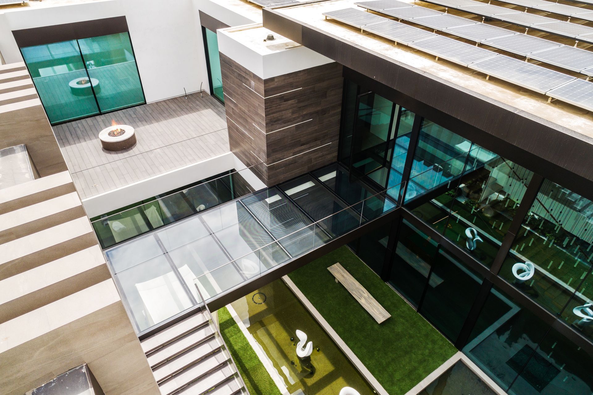 Modern house with glass walls, courtyard, solar panels, and rooftop deck.