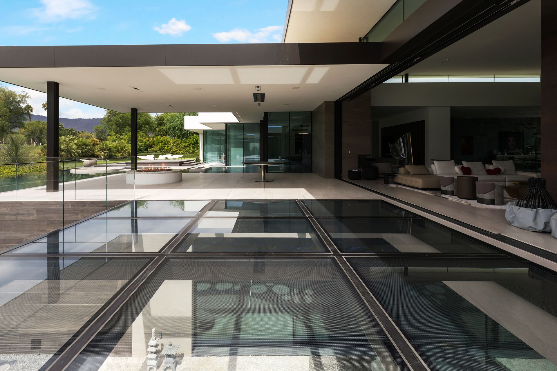 Modern home exterior with glass floor panels, looking into the interior with a view of an outdoor area.