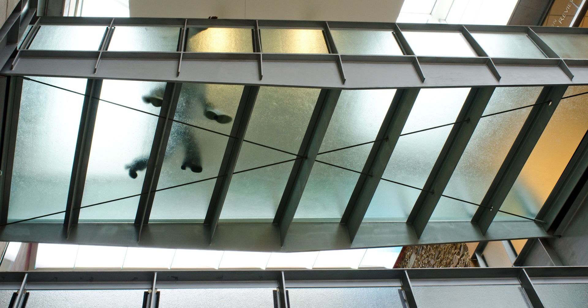 People walking across a glass-floored bridge with a metal support structure.