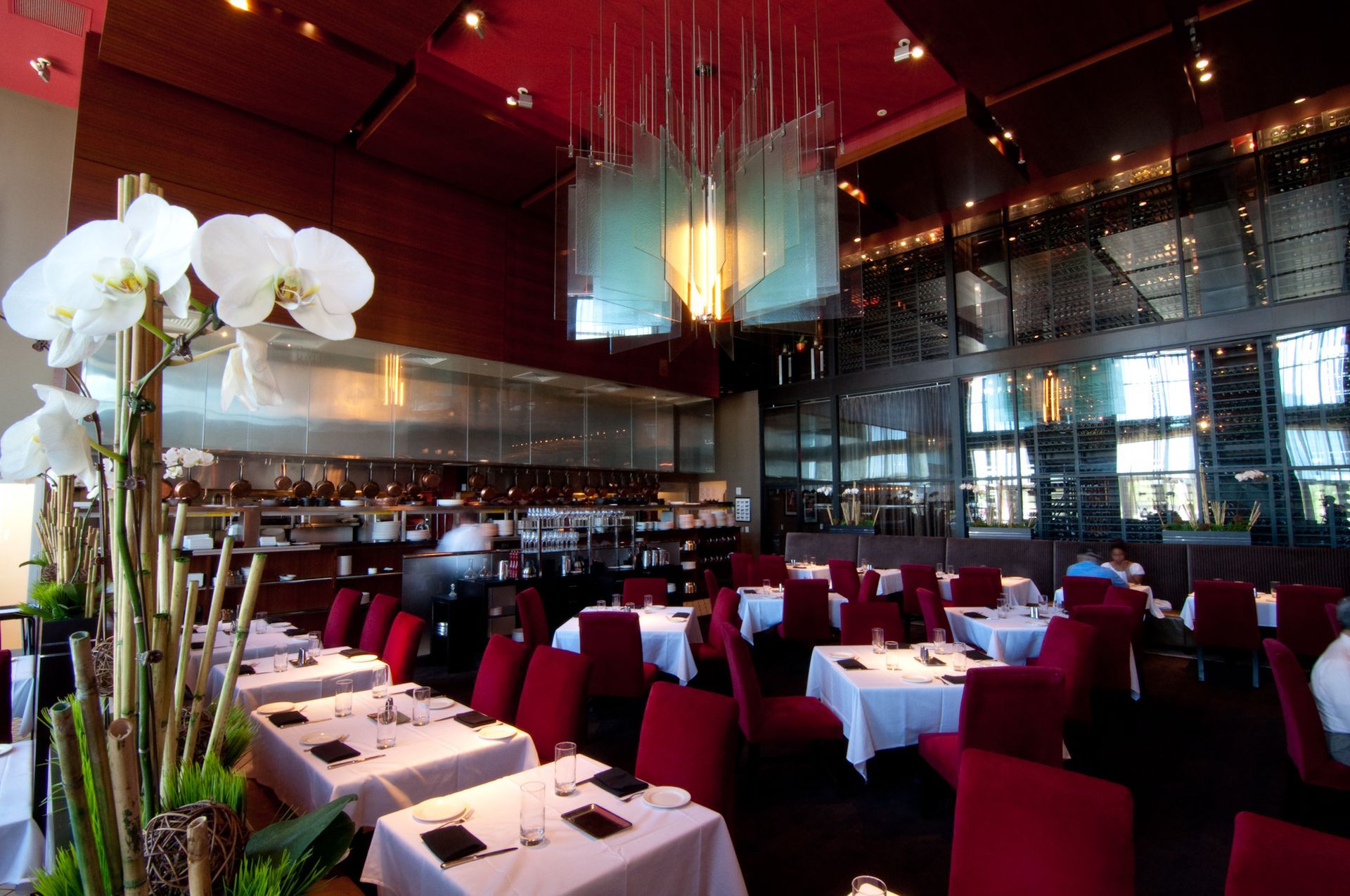 Elegant restaurant dining room with red chairs, white tablecloths, and orchid arrangements under warm lighting