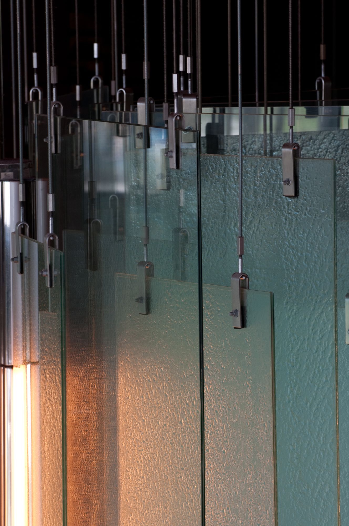 Abstract glass hanging panels with metal rods in a dimly lit interior, softly glowing orange at the bottom