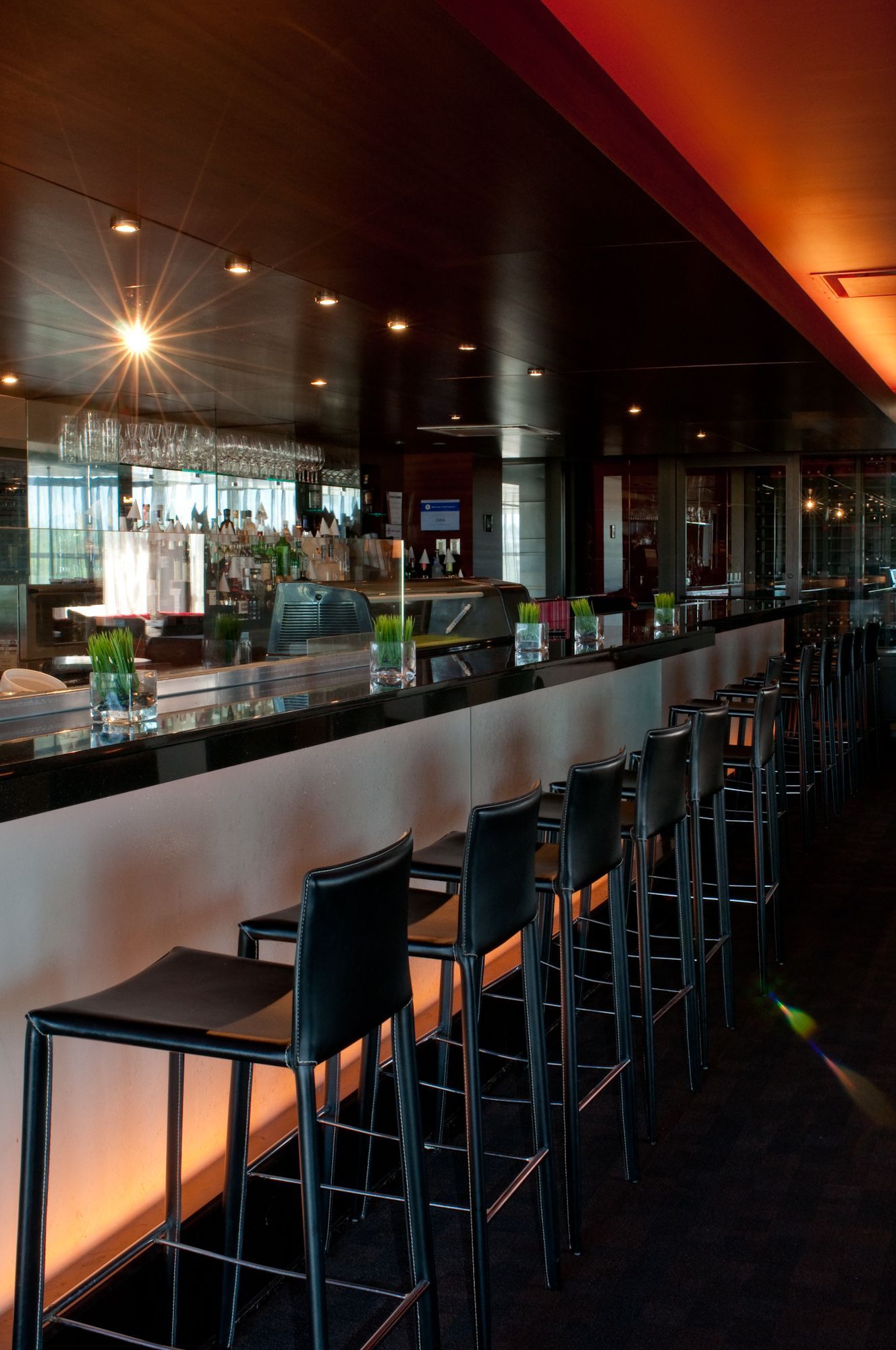 Dimly lit modern bar with a long counter, high stools, and reflections in dark glass walls