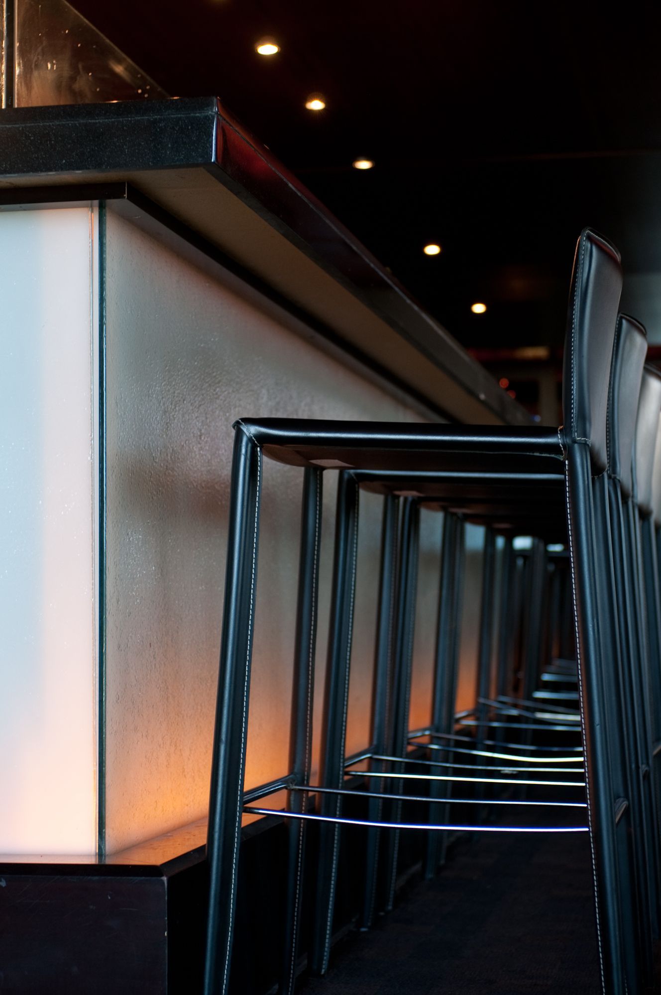 Row of empty bar stools beside a softly lit counter in a dim modern lounge