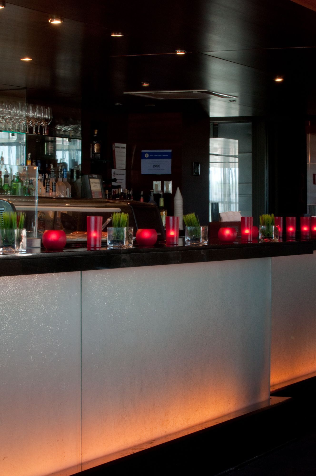 Dimly lit modern bar with glowing red candles along a metallic counter