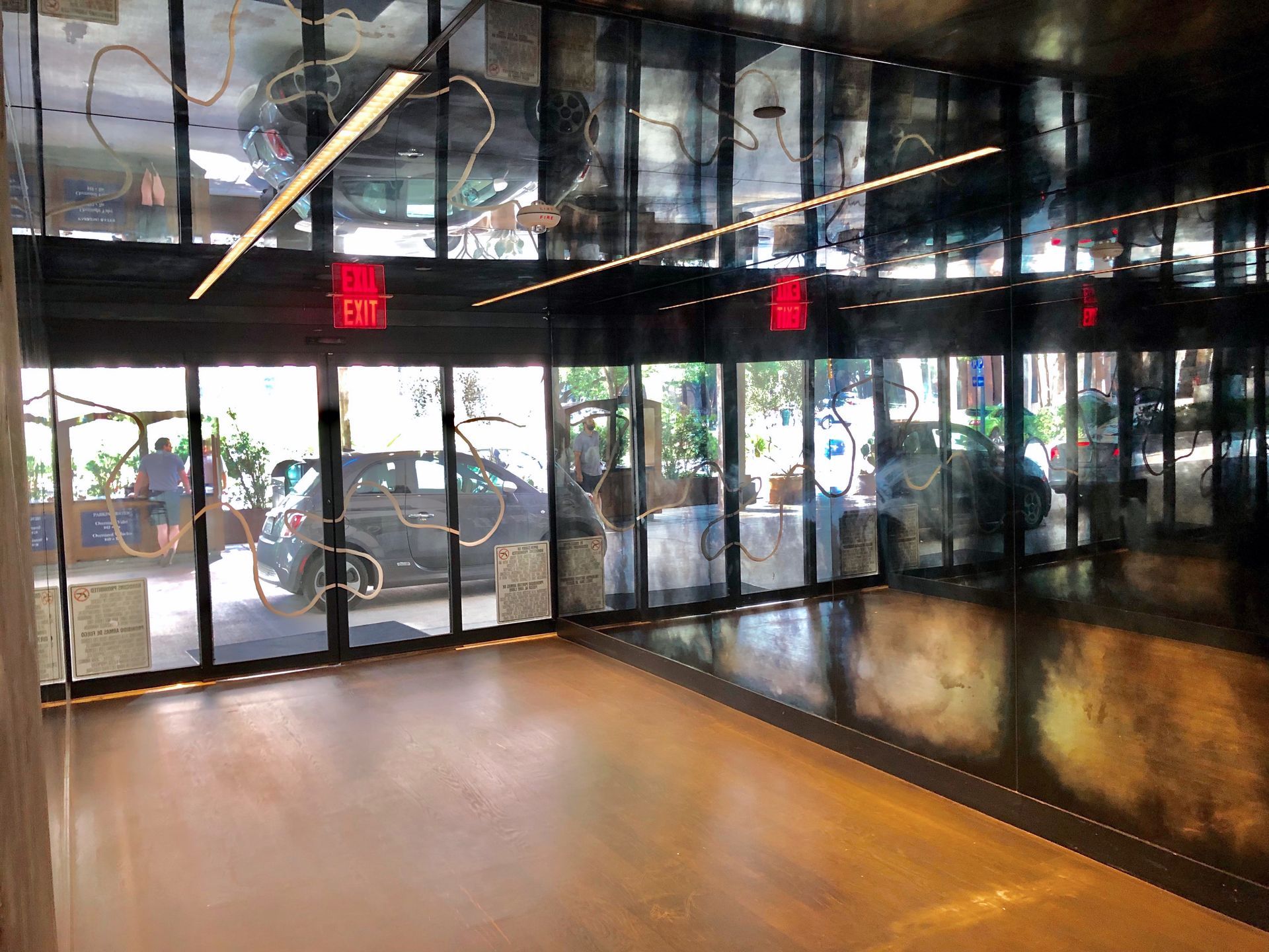 Inside a building with antique mirror ceiling, glass doors, a gray car outside, and an