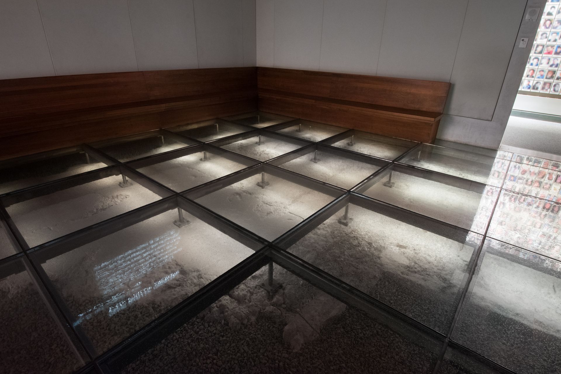 Indoor seating area with wooden benches and a tiled floor covered by a grid of glass panels