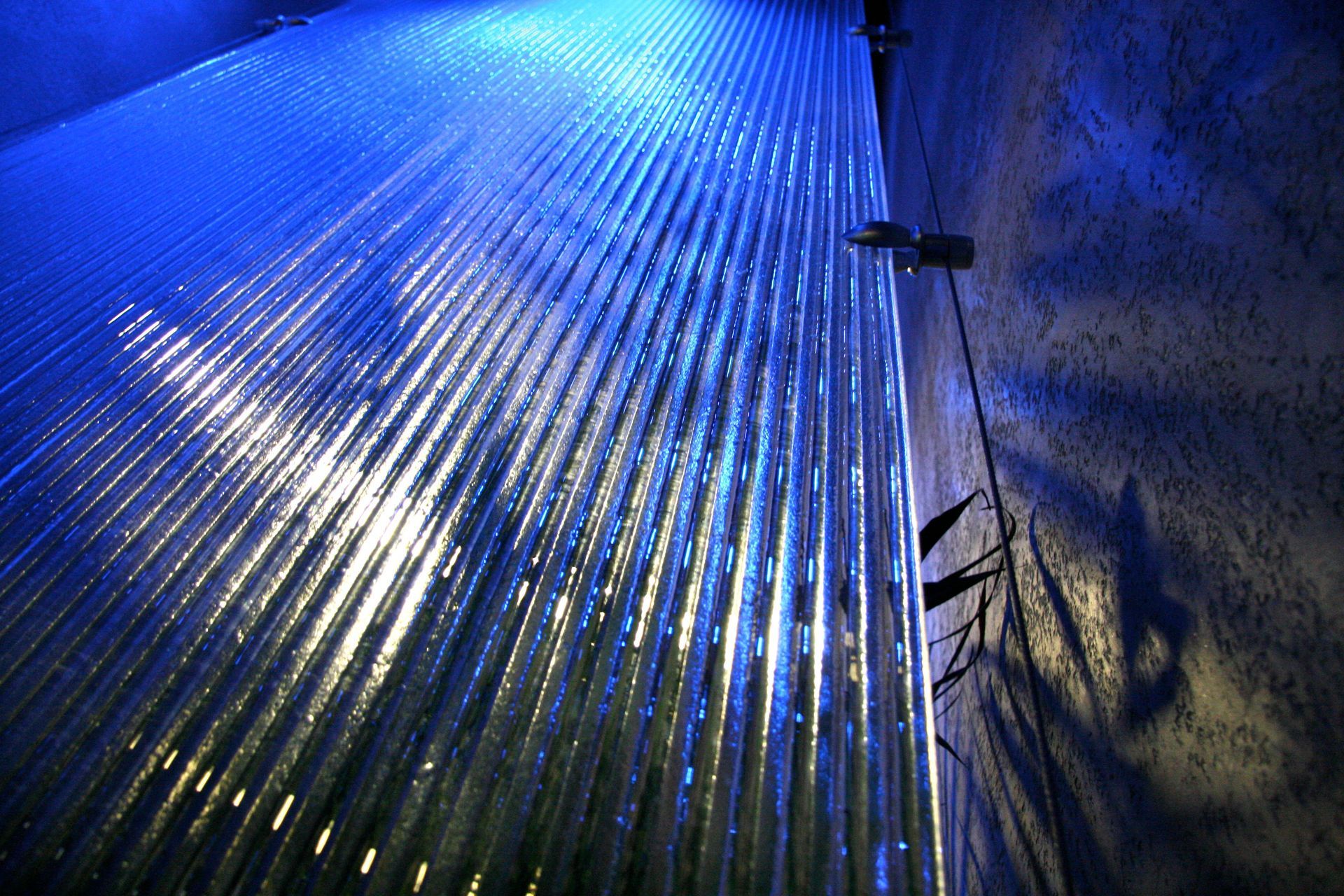 Blue-lit water flows down a textured wall.