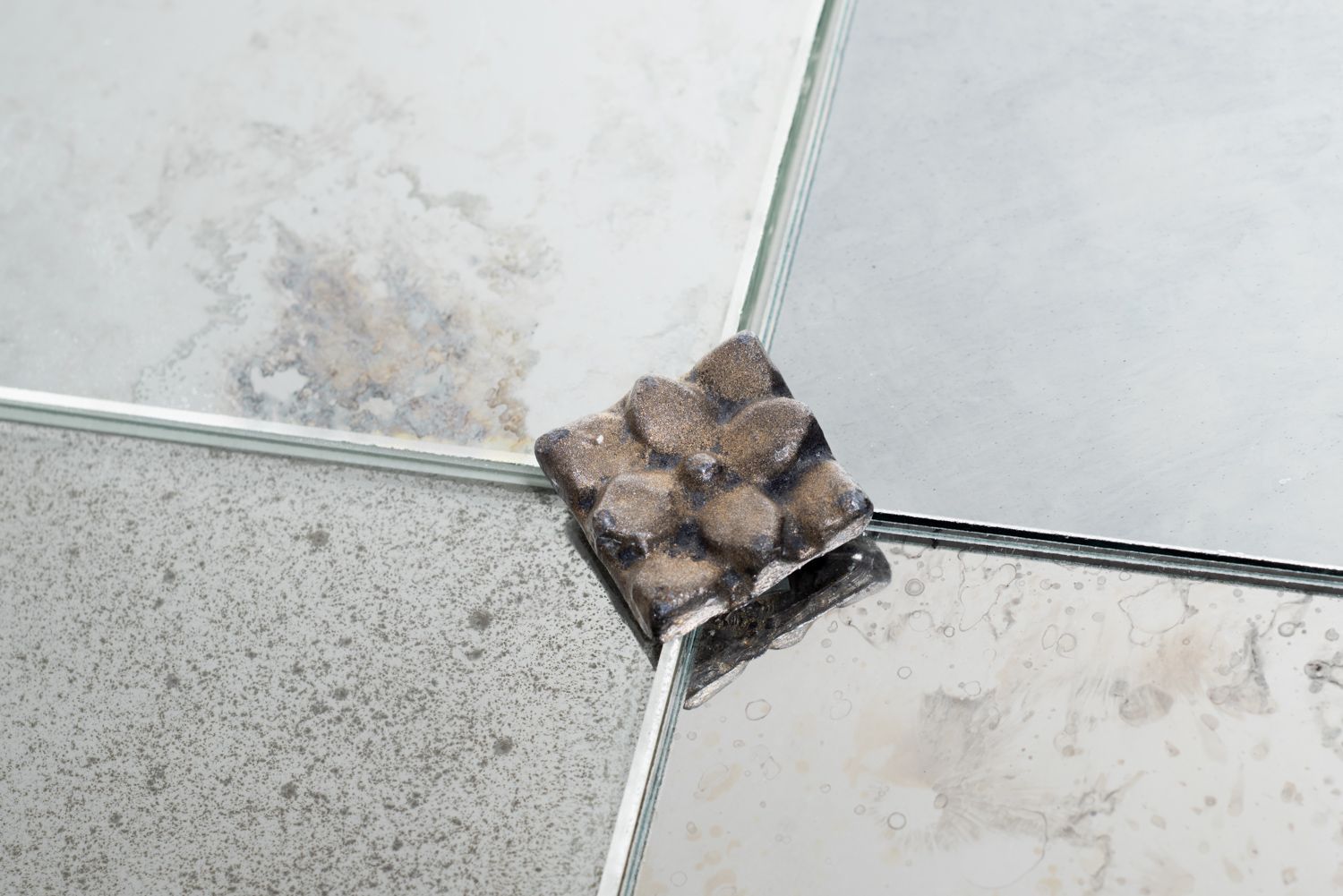 A close-up view of a metal rosette mounting clip securing the corners of four mirrored tiles.