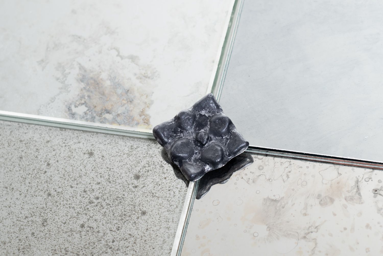 Black melted object at the intersection of two light-colored tiled floor seams