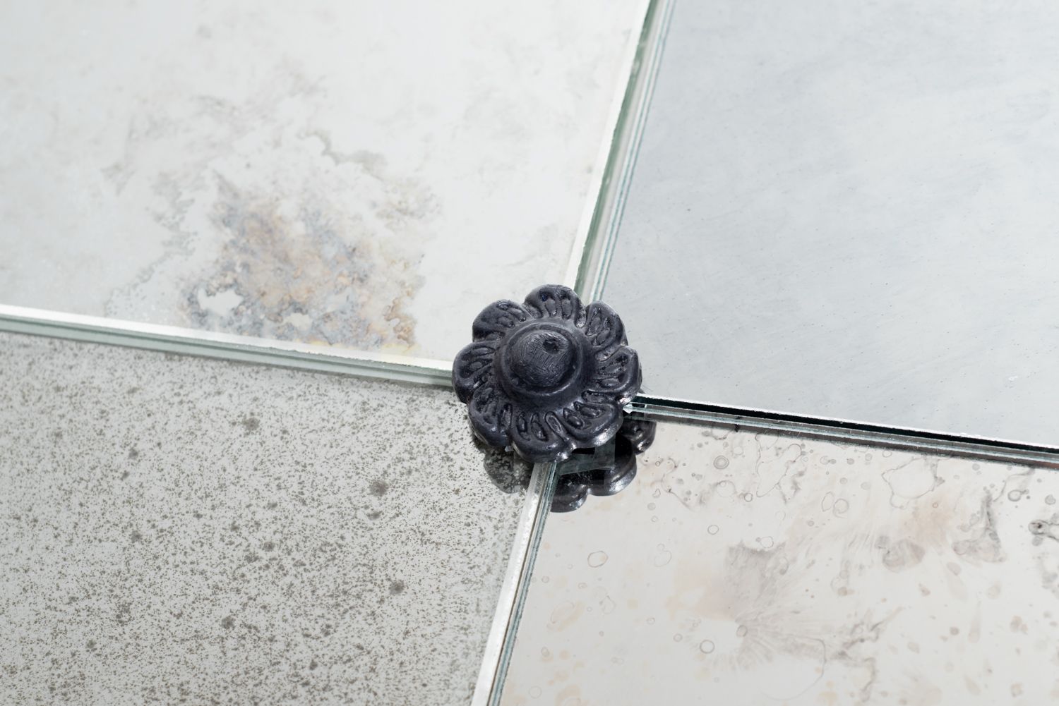 A dark, decorative floral-shaped clamp holds the corners of four glass mirrored tiles together.