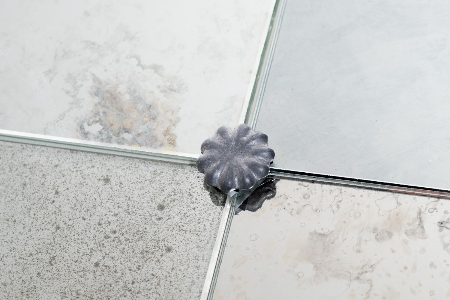 A dark, star-shaped decorative fastener holding four glass mirror panels together at their intersecting corners.