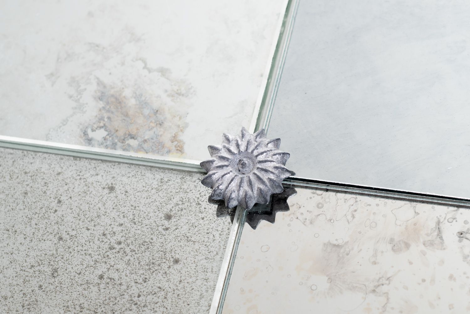 A decorative, flower-shaped metal accent piece sits at the junction of four different types of stone or ceramic tiles.