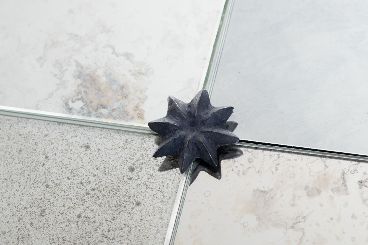 A dark, star-shaped spacer sits at the intersection of four light-colored floor tiles.