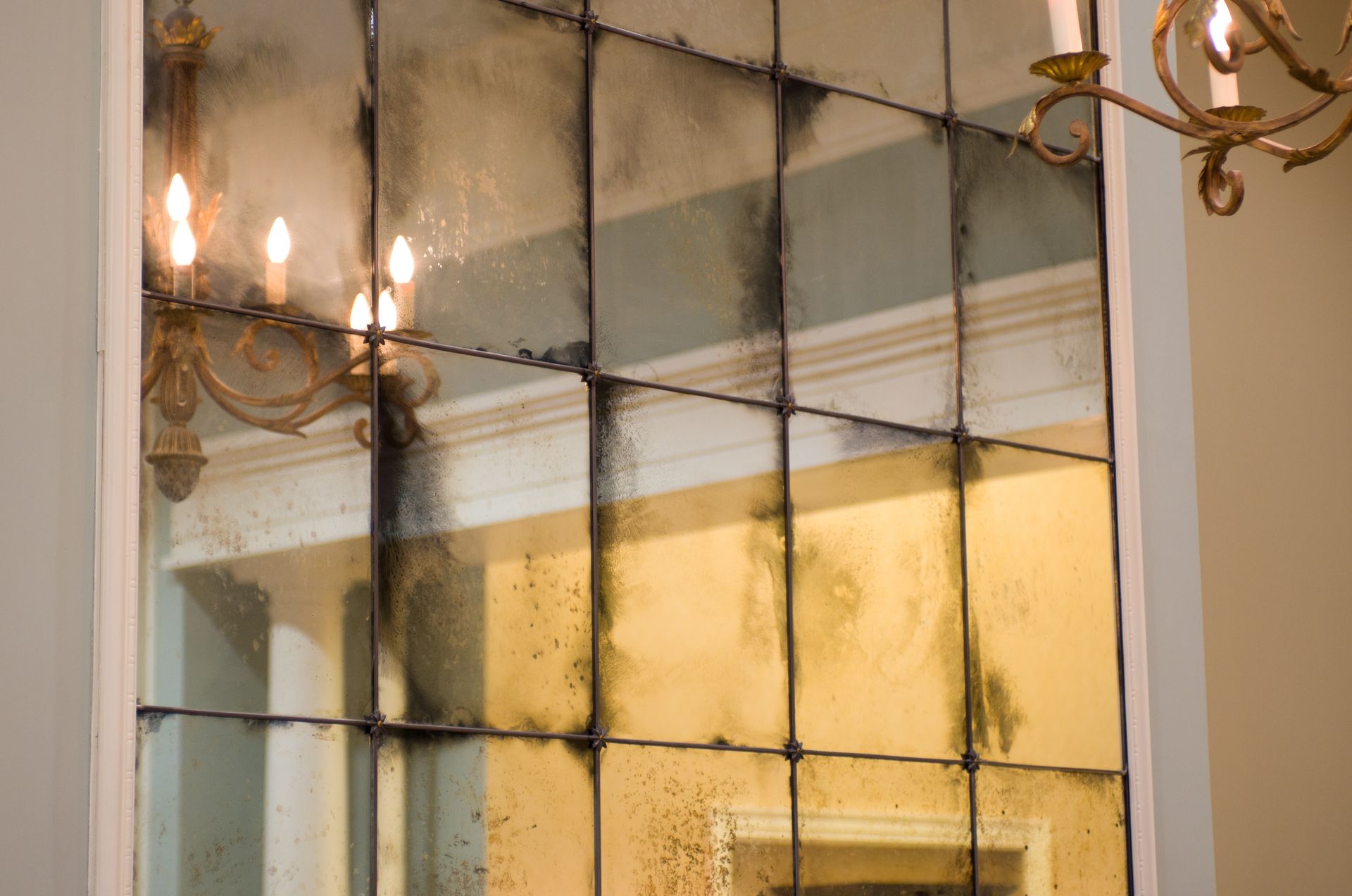 A large antique mirror is hanging on a wall next to a chandelier.
