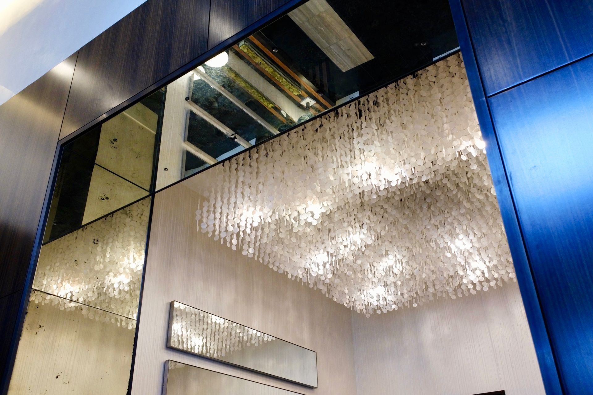 Mirrored wall with large, rectangular chandelier in a modern setting.