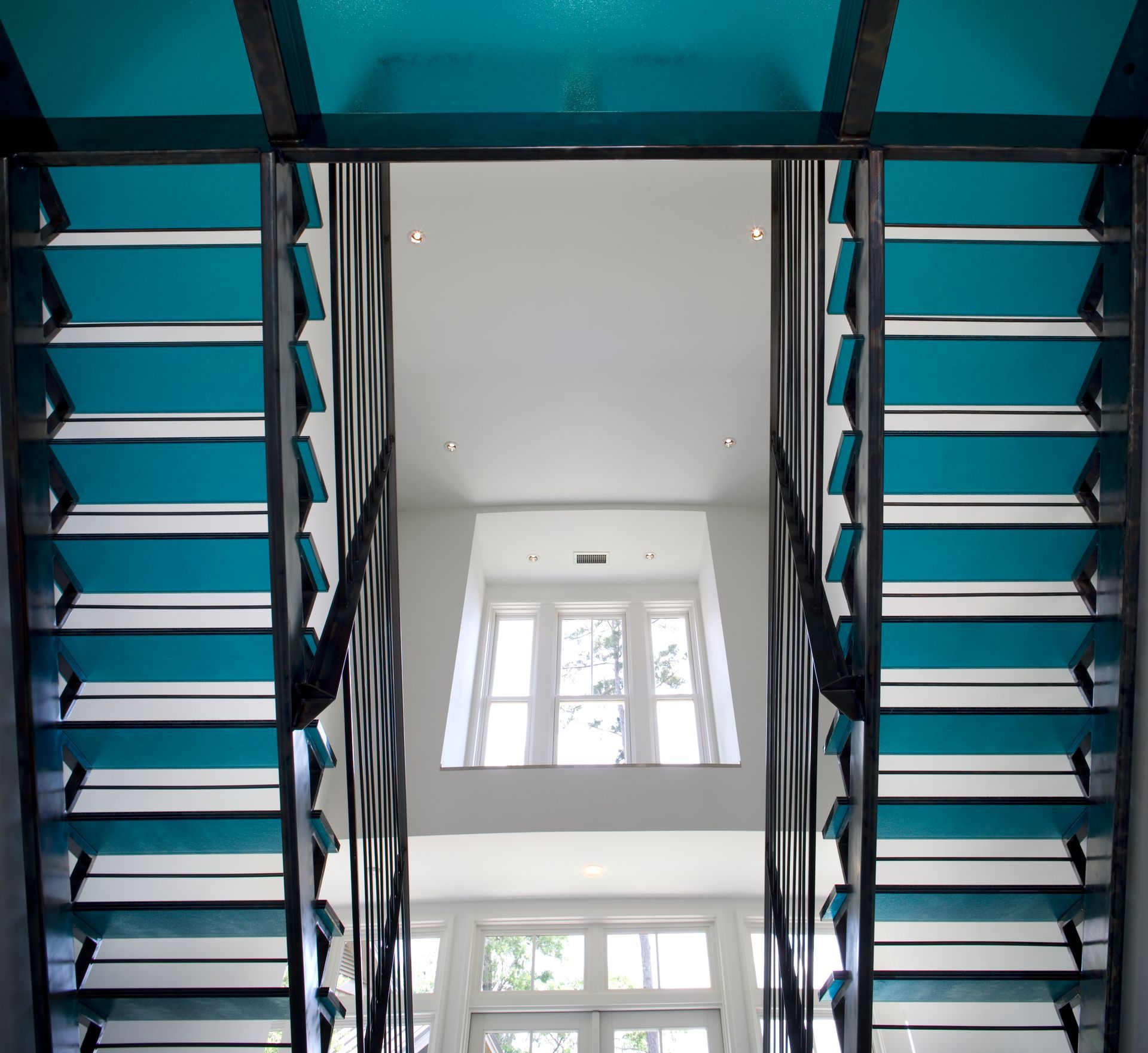 Blue and white interior stairway. Geometric design, large windows at end of hall.
