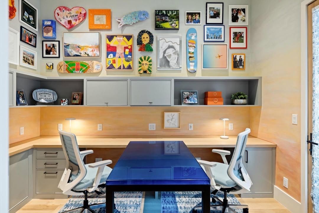 Modern home office with a blue desk, white chairs, and colorful framed wall art