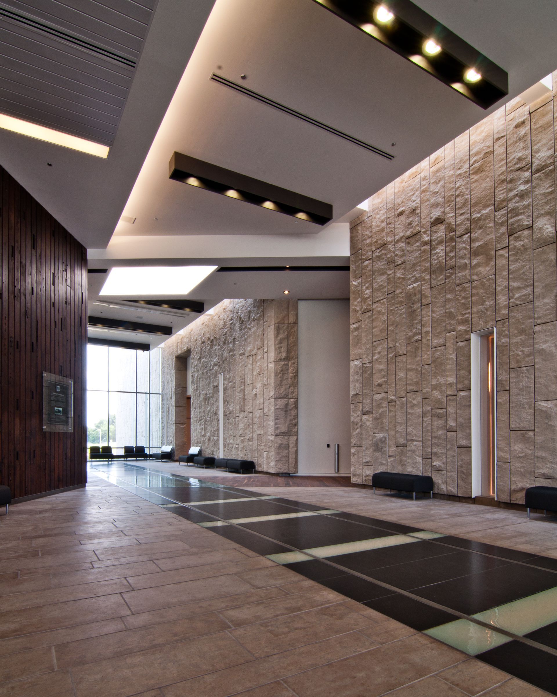 Modern lobby hallway with stone walls, wood floors, skylights, and wall lights