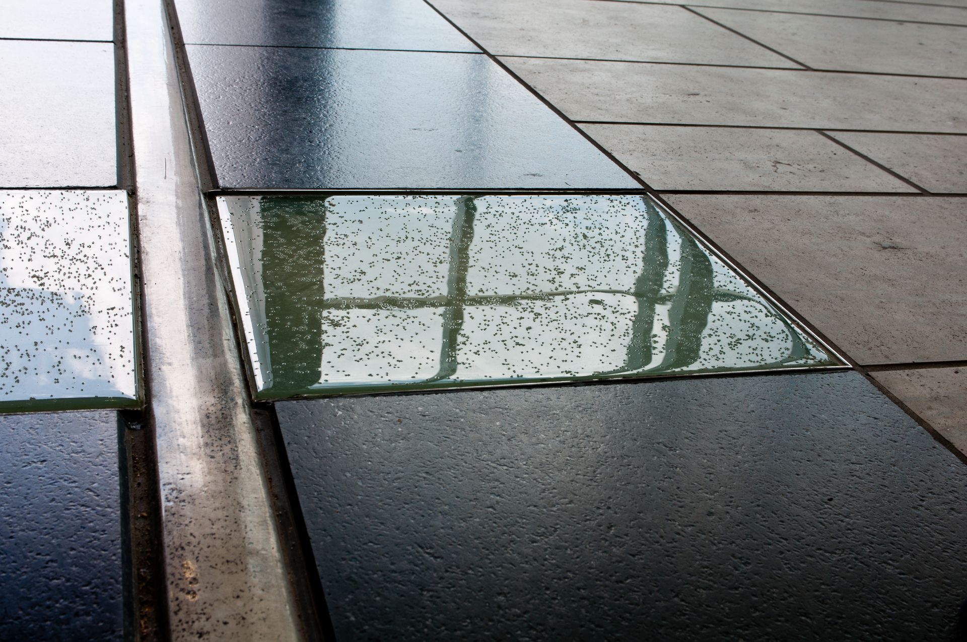 Reflective glass floor panels beside gray stone pavement and a metal curb outdoors