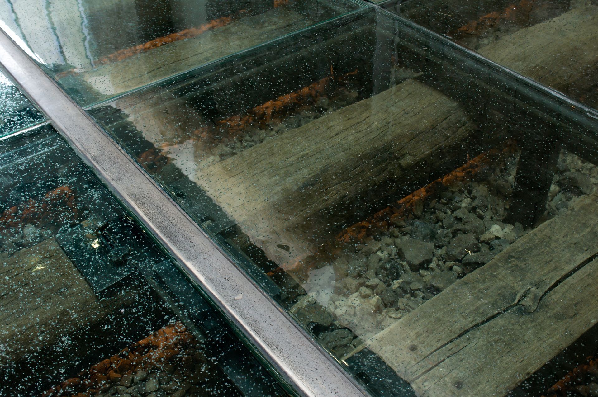 Glass-covered railway tracks with weathered wooden ties and gravel beneath, seen at an angle.