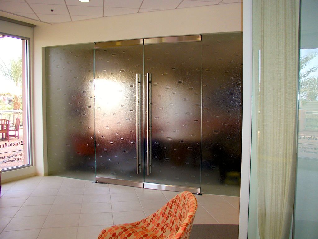 cast glass doors with stainless steel handles in a well-lit room. An orange patterned chair sits in the foreground.