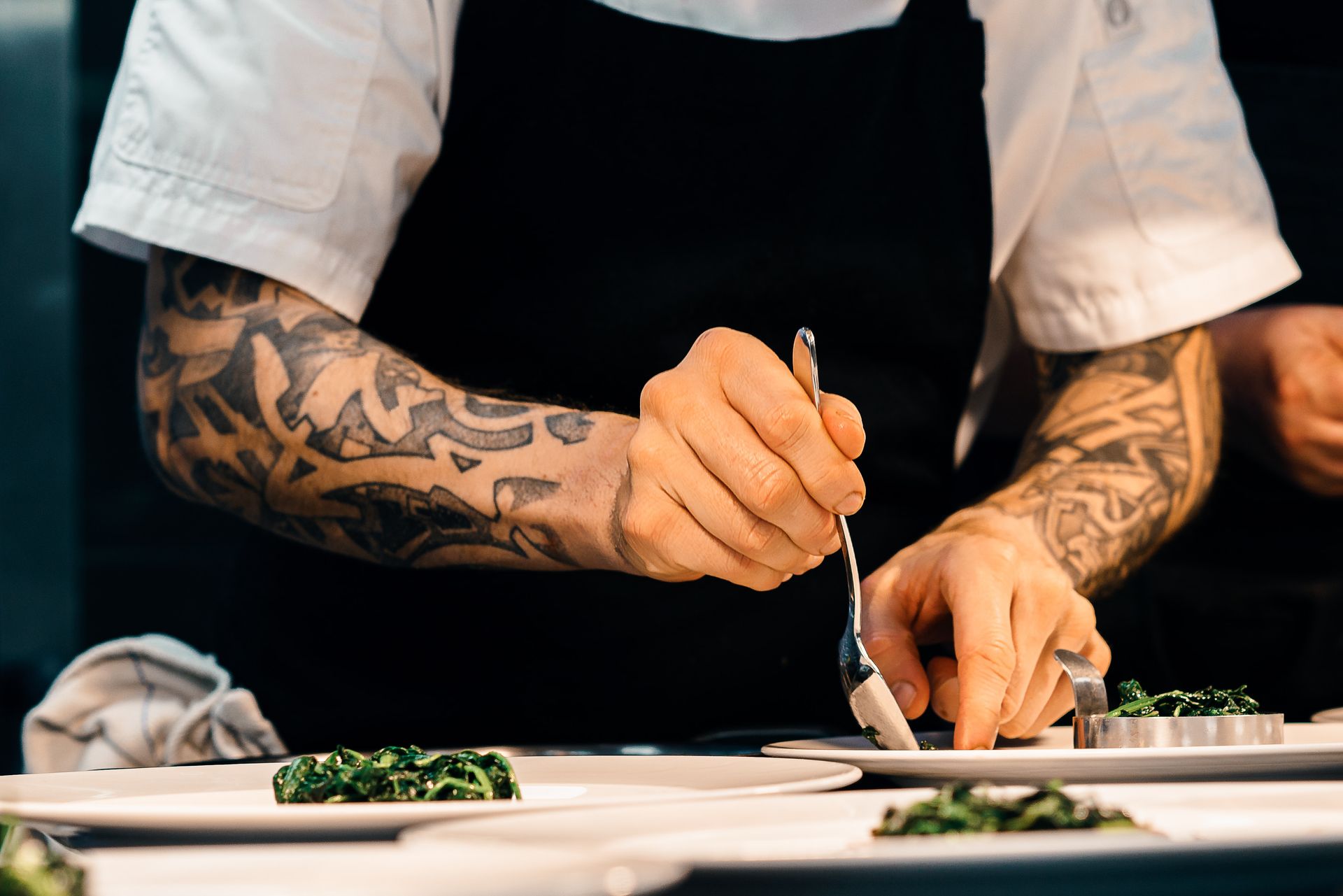 A chef plating greens on white plates A chef plating greens on white plates