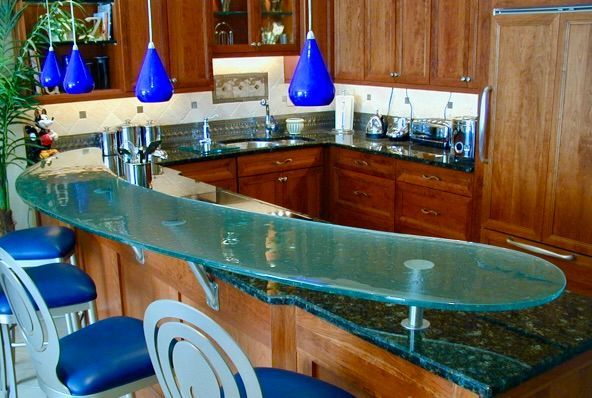 A curved glass countertop bar with blue pendant lights, blue bar stools, and wooden cabinets.