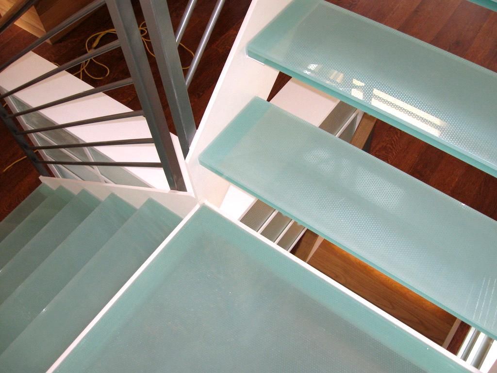 Glass stairs in a modern building, with a metal railing and wooden flooring.