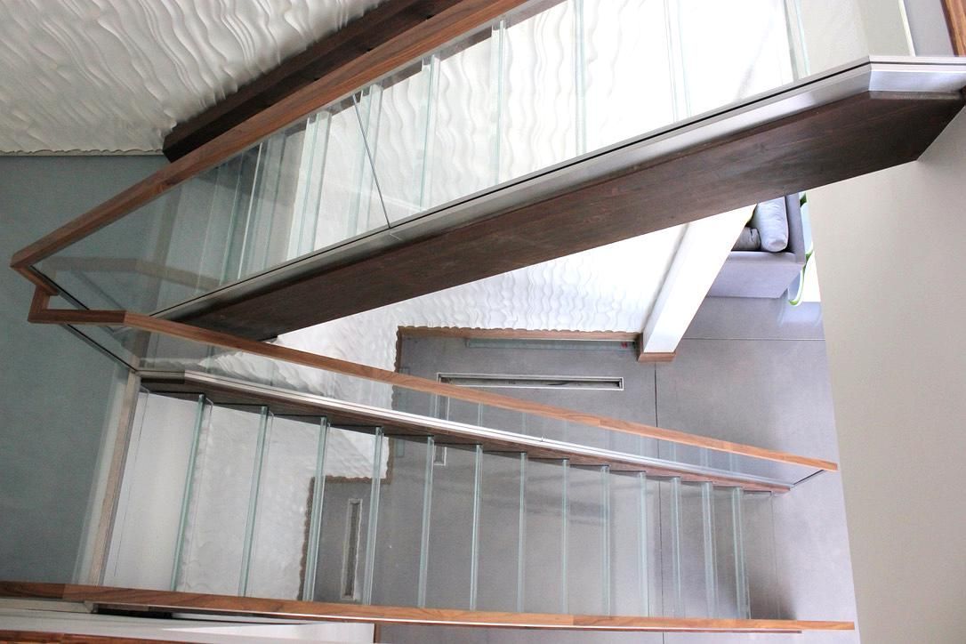 Staircase with glass panels and wooden railings. Light coming from above.