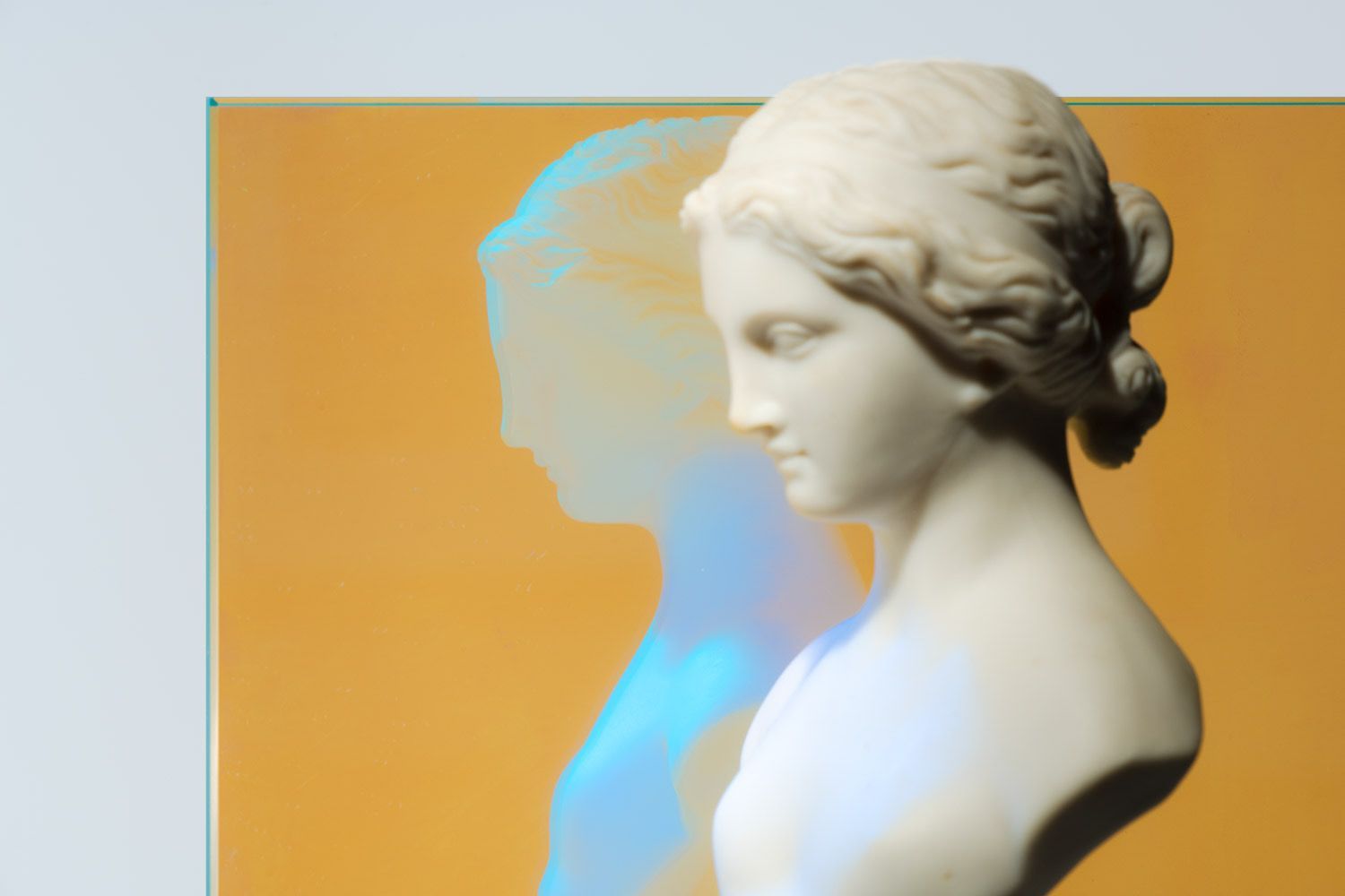 A white bust reflecting against orange dichroic glass. A white bust reflecting against orange dichroic glass.