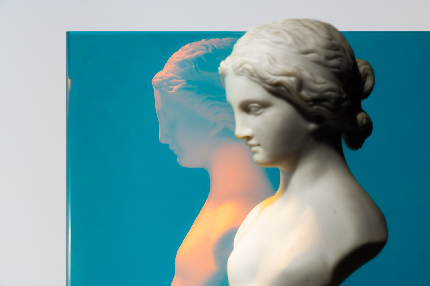A white bust reflecting in a piece of blue dichroic glass.